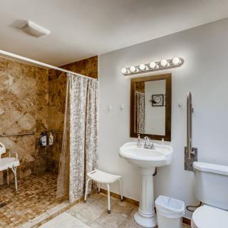A well-lit bathroom with a shower area, pedestal sink, and toilet.