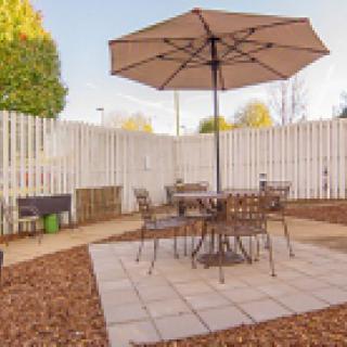 A cozy outdoor patio with a table, chairs, and an umbrella in a fenced backyard.