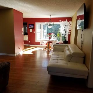 A modern living room with a white couch, dining area, and large windows allowing natural light.
