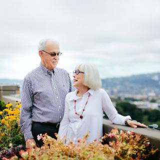 An elderly couple enjoying a scenic view surrounded by flowers.