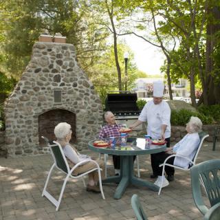 An outdoor dining scene with elderly people being served by a chef in a garden patio setting.