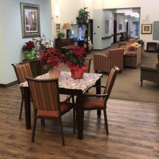 A cozy indoor lounge area with tables, chairs, and sofas, decorated with plants and paintings.