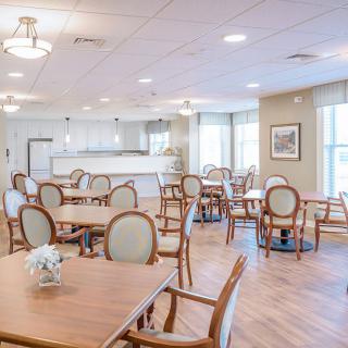 A modern and bright dining area with neatly arranged tables and chairs, featuring large windows.