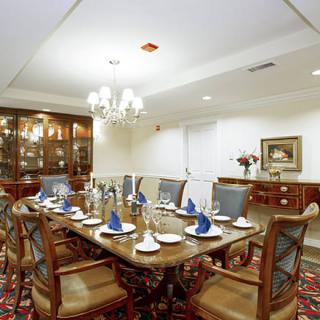 An elegantly set dining room with a polished wooden table, blue napkins, and a chandelier overhead.