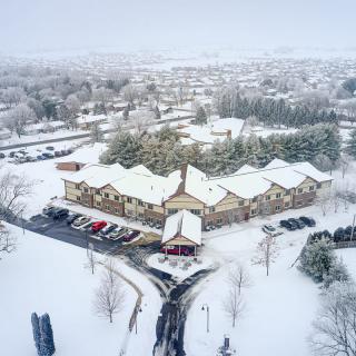 Aerial view of a snowy neighborhood with houses and trees blanketed in white on an overcast day.