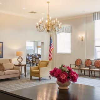A well-furnished living room with a chandelier, comfortable seating, and a vase of flowers on the table.
