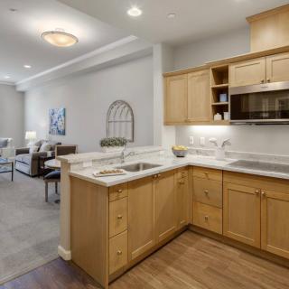 A modern kitchen with wooden cabinets opens into a living room, showcasing an open floor plan in an apartment interior.