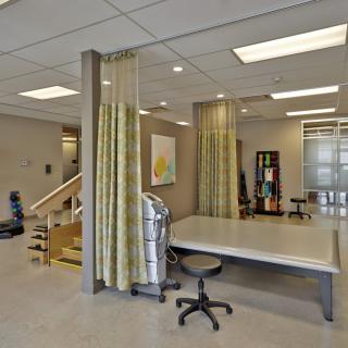 A rehabilitation center with a treatment area featuring exercise equipment and privacy curtains.