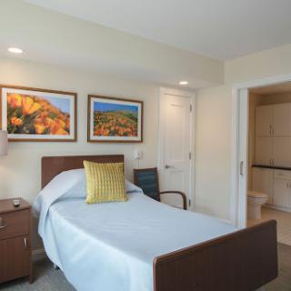A cozy bedroom featuring a single bed, decorative pillows, and artwork on the walls, with an adjoining bathroom.