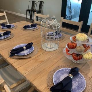A dining table is elegantly set with purple plates, dark napkins, and a centerpiece featuring a decorative birdcage and seasonal pumpkins.