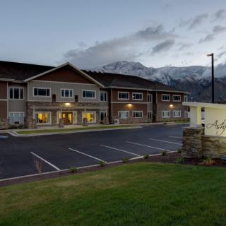 A hotel building with a parking lot in front and mountains in the background during the evening.