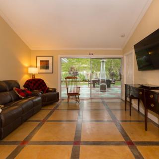 A cozy living room with a sofa, wall-mounted television, and large glass doors leading to an outdoor patio.