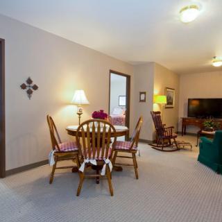 A cozy living and dining area featuring a wooden table with chairs, lamps, and a television in the background.