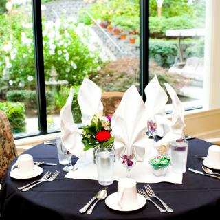 An elegantly set dining table with folded white napkins, colorful flowers, and glassware against a backdrop of a lush outdoor view.