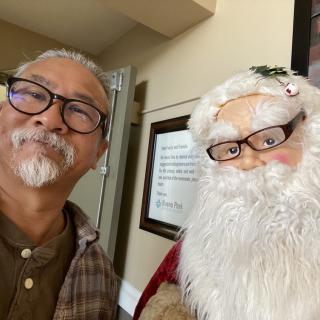 A person poses for a selfie with a Santa Claus figure indoors.