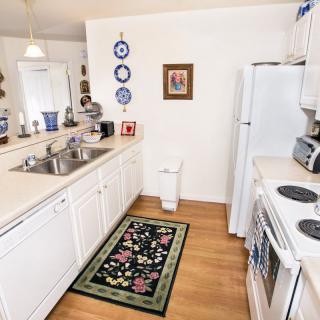 A bright kitchen with white cabinets, decorated plates, and a colorful rug on a wooden floor.
