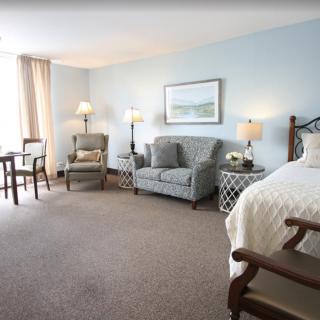 A spacious and well-decorated hotel room with a bed, sofa, armchair, and ample lighting.