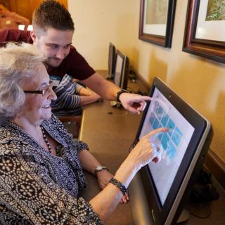 An elderly woman learns to use a computer with the assistance of a younger person.