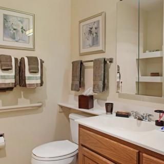 A neatly organized bathroom with hanging towels, a mirror, and decorative artwork.
