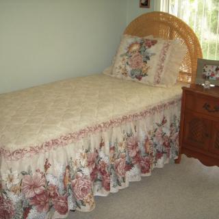 A cozy bedroom with a single bed featuring floral bedding and a wooden headboard, accompanied by a wooden nightstand.