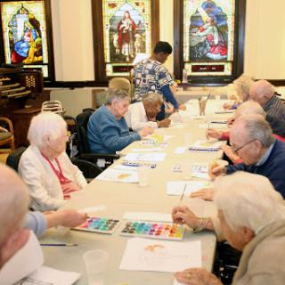 A group of elderly individuals engaged in a creative activity at a community center, surrounded by beautiful stained glass windows.