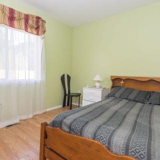 A cozy bedroom with a wooden bed, nightstand, and a chair by the window.
