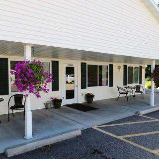 The front entrance of a building with a covered porch, chairs, and hanging flower pots.