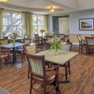 A cozy dining area with tables and chairs arranged neatly, decorated with fresh flowers.