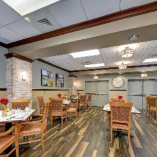 A well-decorated dining area with multiple tables and chairs, featuring wood flooring and elegant lighting.