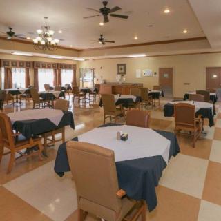 A spacious and well-lit dining area with neatly arranged tables and chairs, featuring ceiling fans and decorative lighting.