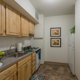 A compact kitchen with wooden cabinets, a stove, and decorative wall art.