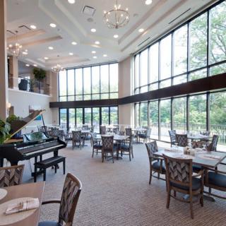 A modern dining area with large windows, a piano, and elegant chandeliers.