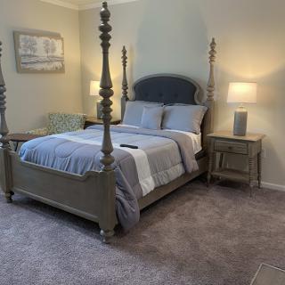 A cozy bedroom with a four-poster bed, matching nightstands with lamps, and soft carpeting.