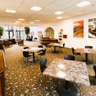 A modern indoor cafeteria with marble tables and black chairs, featuring artwork on the walls and a carpeted floor.