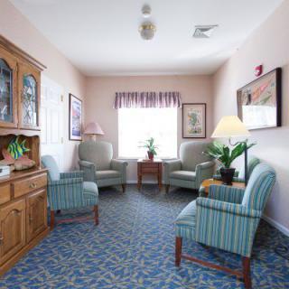 A cozy living room with comfortable chairs and a cabinet, featuring indoor plants and decorations.