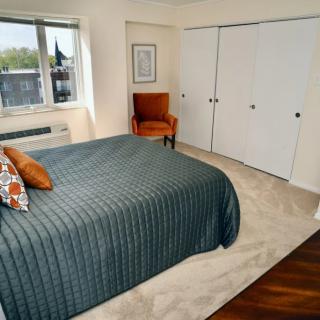 A cozy bedroom featuring a neatly made bed, an orange chair by the window, and a spacious closet with white doors.