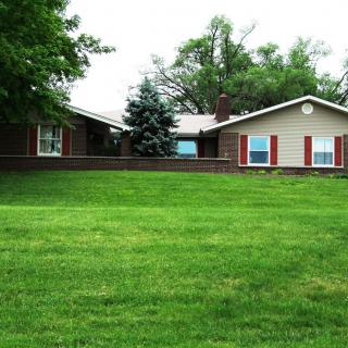 A suburban house with a large green lawn and surrounding trees.