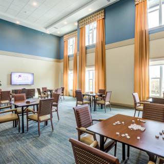 A spacious room with several tables and chairs, large windows with curtains, and a wall-mounted television.