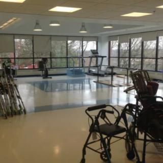 A rehabilitation room equipped with exercise machines, walkers, and wheelchairs.