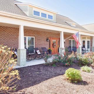 A brick house with a spacious front porch featuring chairs, an American flag, and well-maintained landscaping.