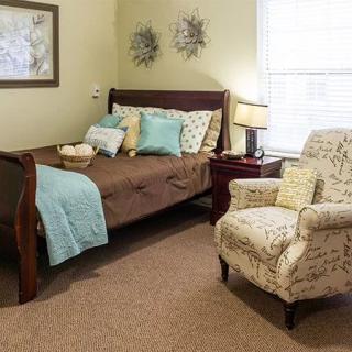 A cozy bedroom featuring a bed with blue and brown bedding, an armchair, and a bedside lamp.
