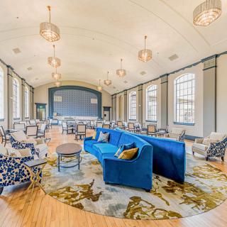 A spacious and modern lounge area featuring a blue couch, large windows, and contemporary lighting.