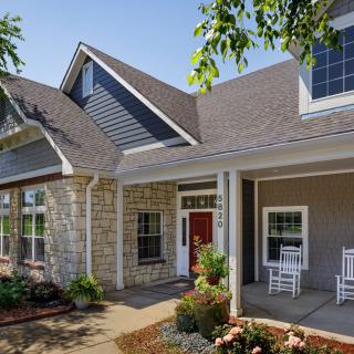 A modern house with a stone facade, featuring a red door and a welcoming porch.