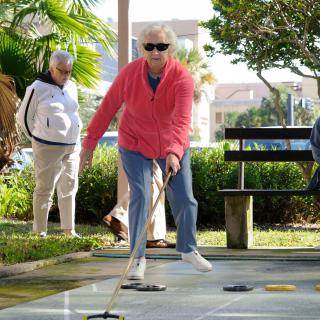 A senior woman enjoying a game of shuffleboard outdoors on a sunny day.