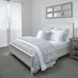 A neatly arranged bedroom featuring a bed with patterned bedding, a nightstand, and natural lighting from the window.