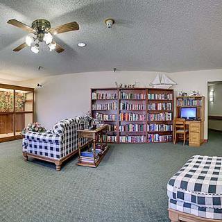 A cozy living room featuring a large bookshelf, plaid sofas, and a ceiling fan.