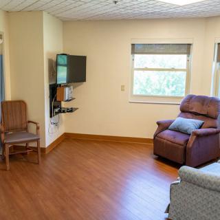 A cozy living room with a recliner, chair, television, and a window with natural light.