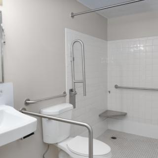 An accessible bathroom featuring a toilet, sink, and shower with grab bars for support.