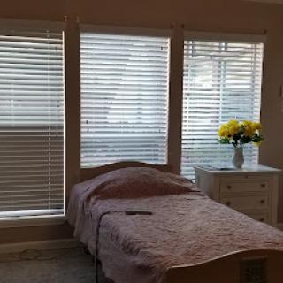 A cozy bedroom with natural light filtering through the blinds and a vase of flowers on the nightstand.