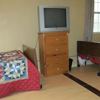 A cozy bedroom featuring a wooden dresser, a quilted bedspread, and an older television set.